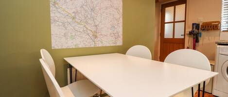 Un comedor con una mesa y sillas blancas, un mapa en la pared y una lavadora al fondo.