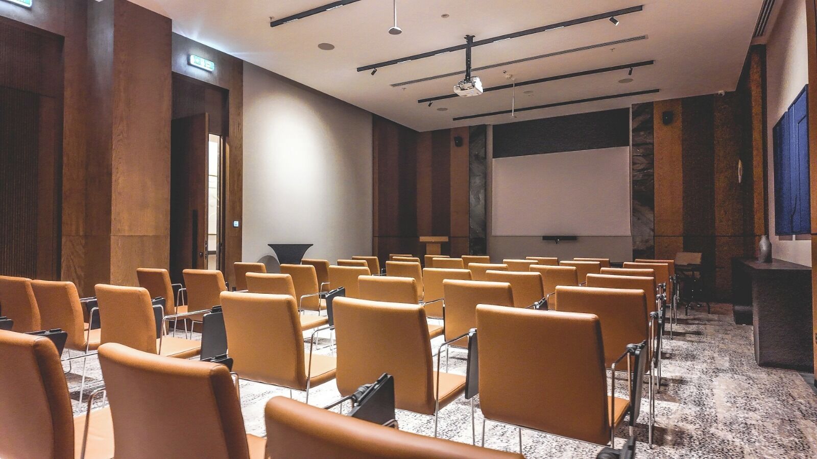A conference room with rows of chairs, a projector screen, and a podium.