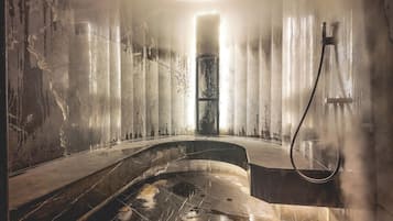 Ein schwach beleuchtetes Badezimmer im Industriedesign mit einer großen Badewanne, einer Duschkabine und freiliegenden Rohren.