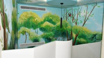 Habitación con un mural de un paisaje forestal, un banco curvo blanco y una lámpara en el techo.