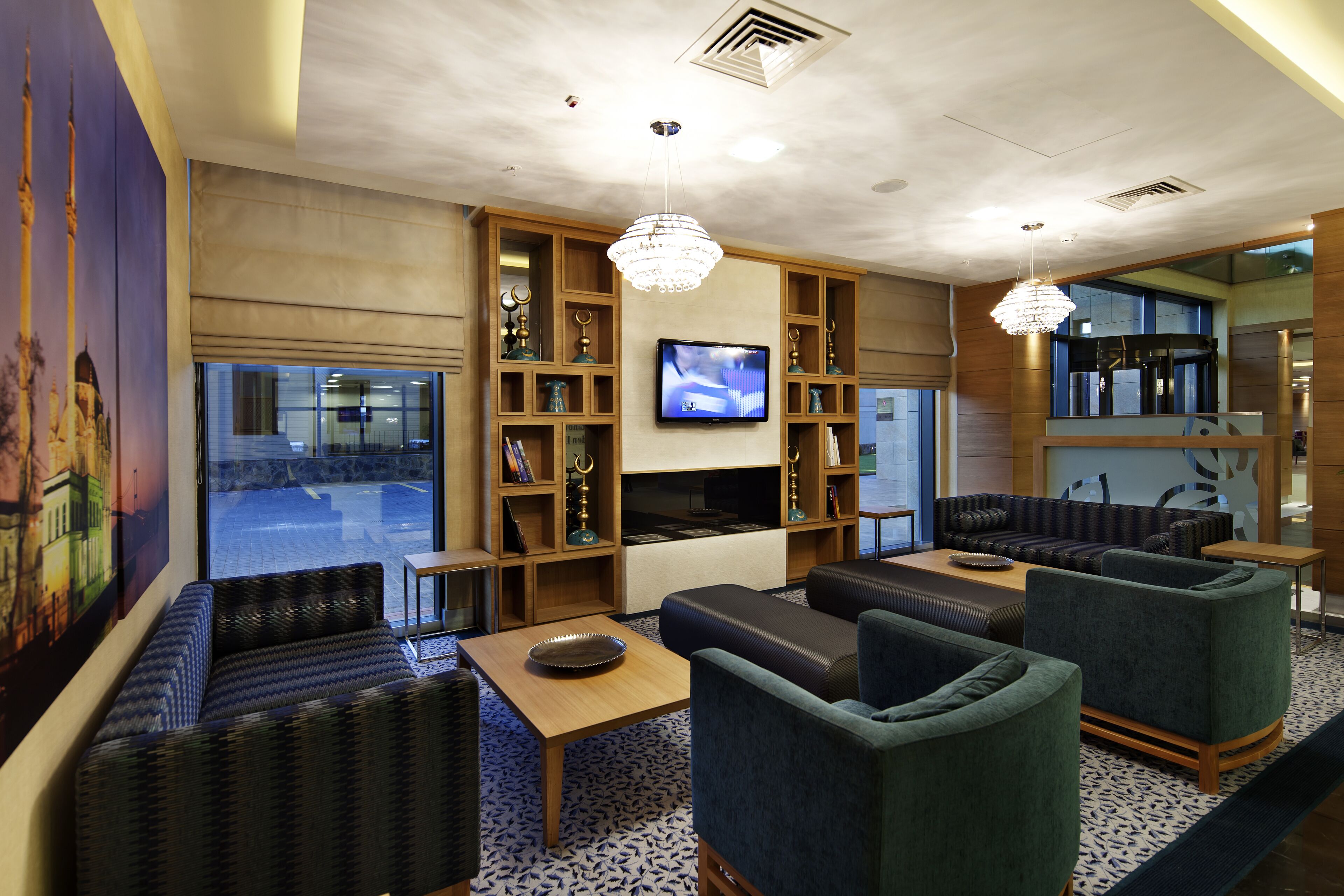A modern hotel lobby with seating areas, a television, and decorative shelves.