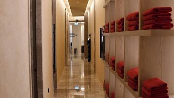 Un couloir d’hôtel avec un sol en marbre, des étagères en bois où sont pliées des serviettes rouges, et un design épuré et moderne.