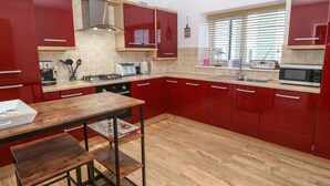 Una cocina moderna con armarios rojos, una mesa de madera y una ventana con persianas.