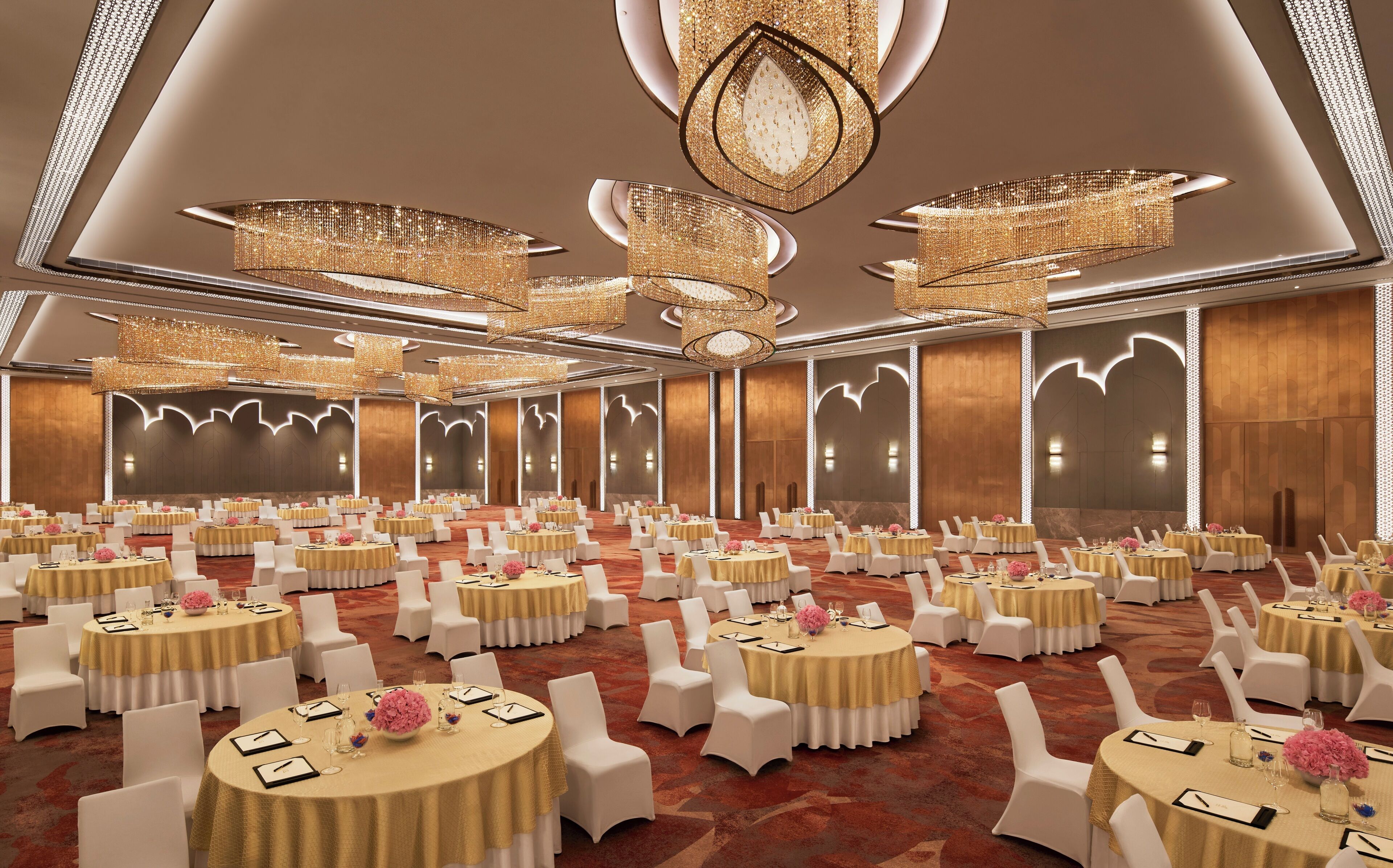 A banquet hall with round tables, white chairs, and gold tablecloths.
