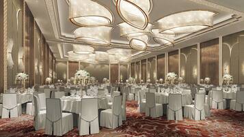 A banquet hall with round tables, white chairs, and floral centerpieces.