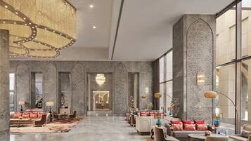 A spacious lobby with a high ceiling, marble walls, and a central chandelier. There are seating areas with sofas and tables, and large windows providing natural light.