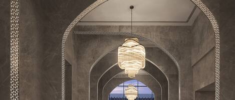 A corridor with arches and a chandelier, leading to a view of a building.