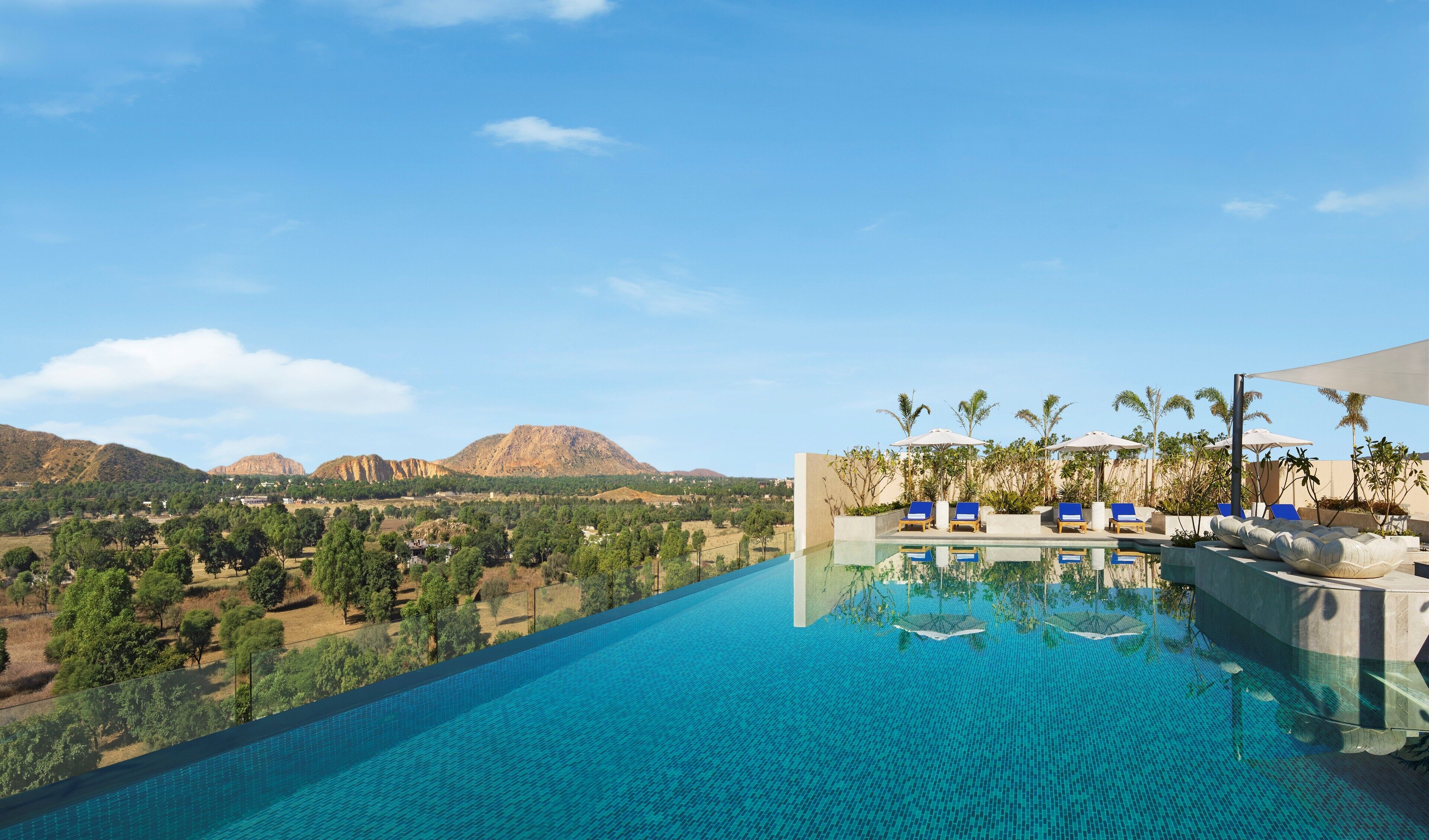A pool with clear blue water, surrounded by lounge chairs and umbrellas, with a view of mountains and greenery in the background.