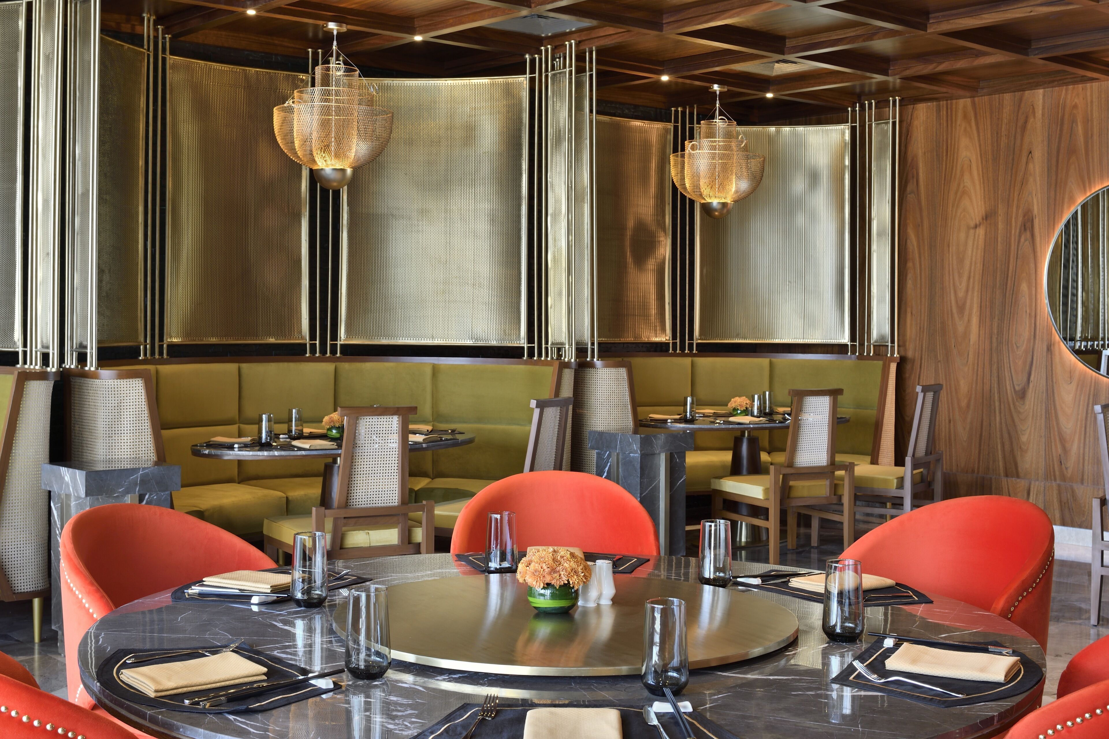 A restaurant with round tables, red chairs, and hanging chandeliers.