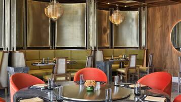 A restaurant with round tables, red chairs, and hanging chandeliers.