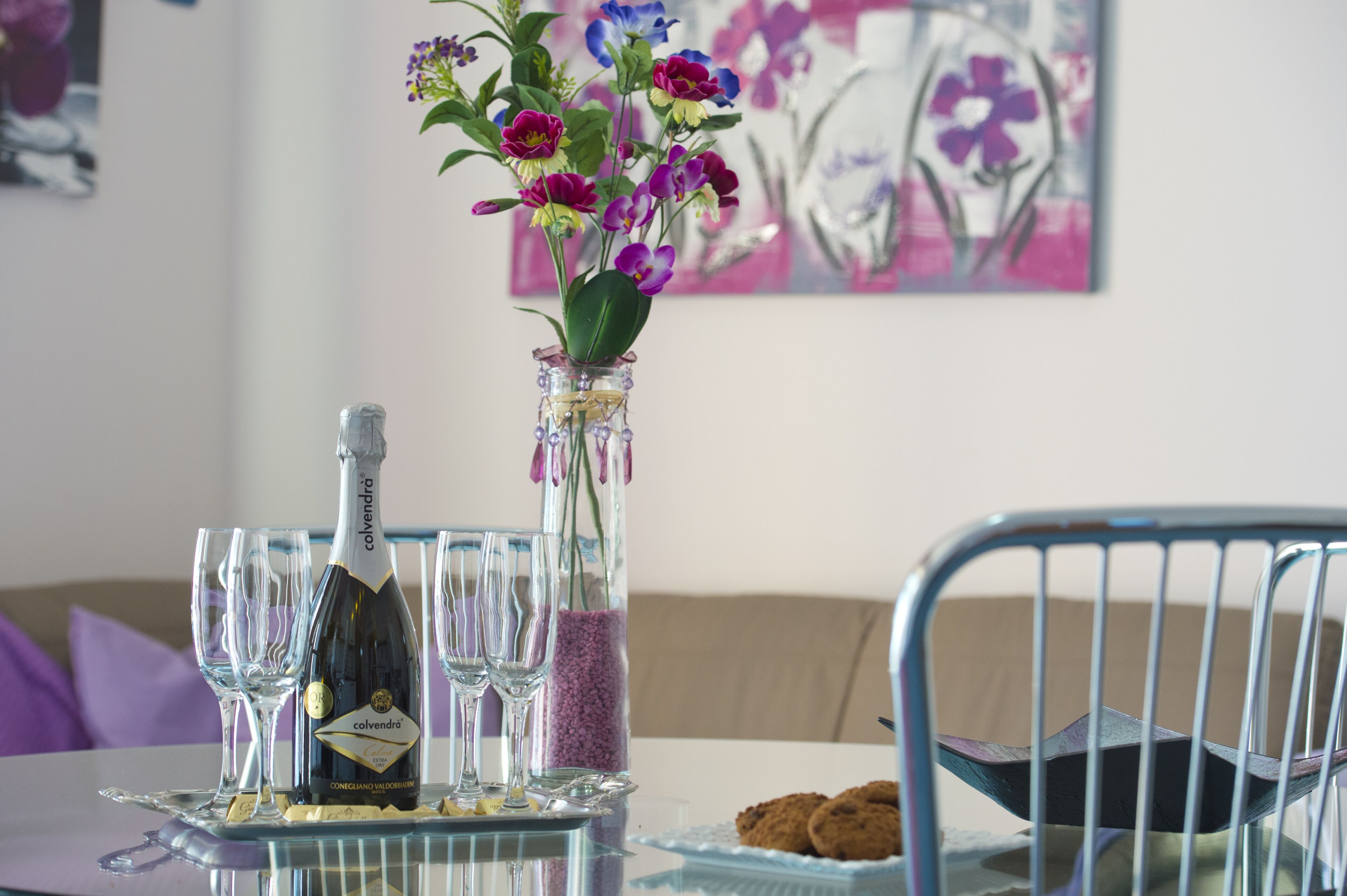 A table with a bottle of champagne, a vase with flowers, and several glasses.