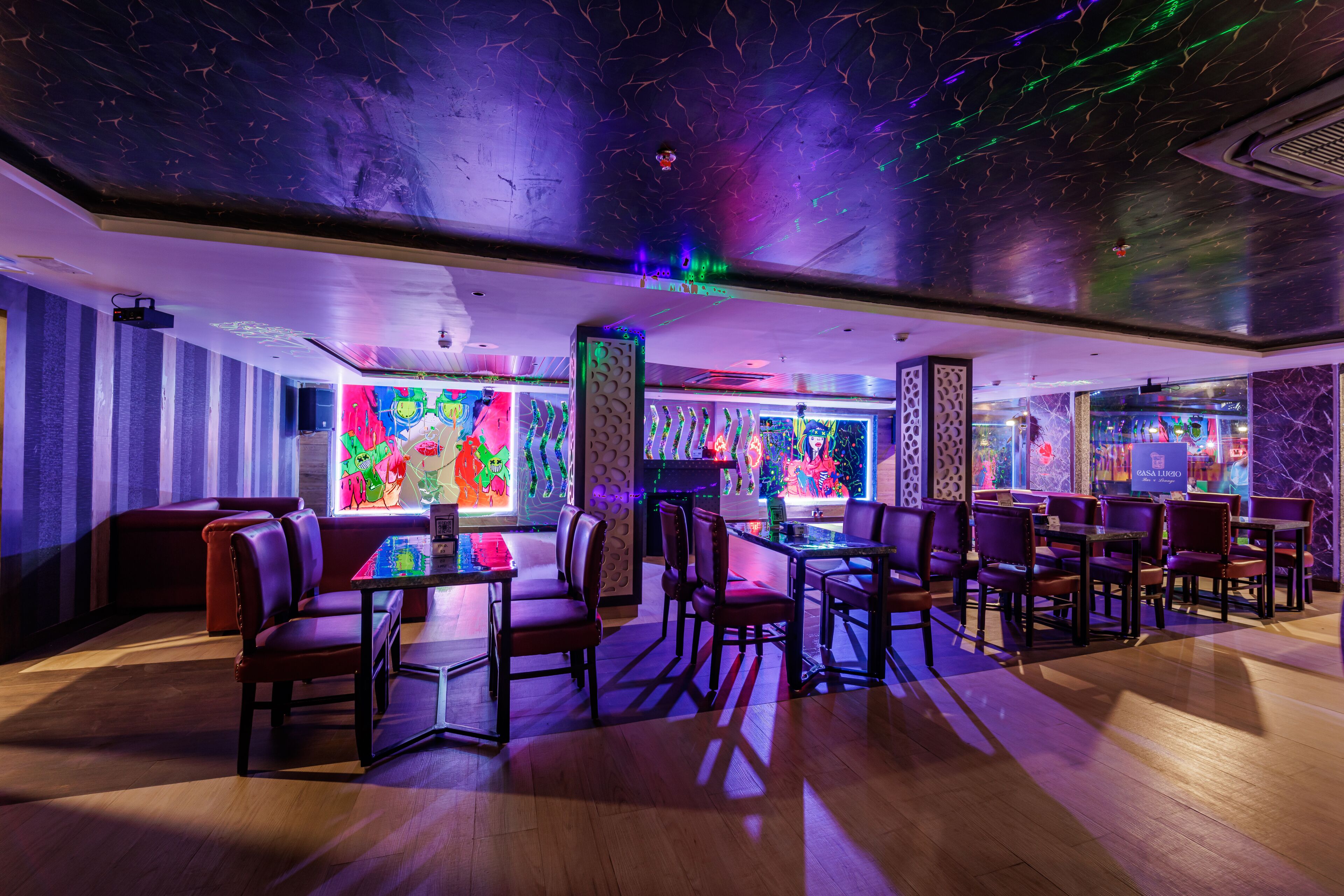 Un restaurante con cabinas y mesas, arte murales coloridos y un techo con diseños de luces.