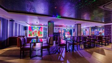 Un restaurante con cabinas y mesas, arte murales coloridos y un techo con diseños de luces.