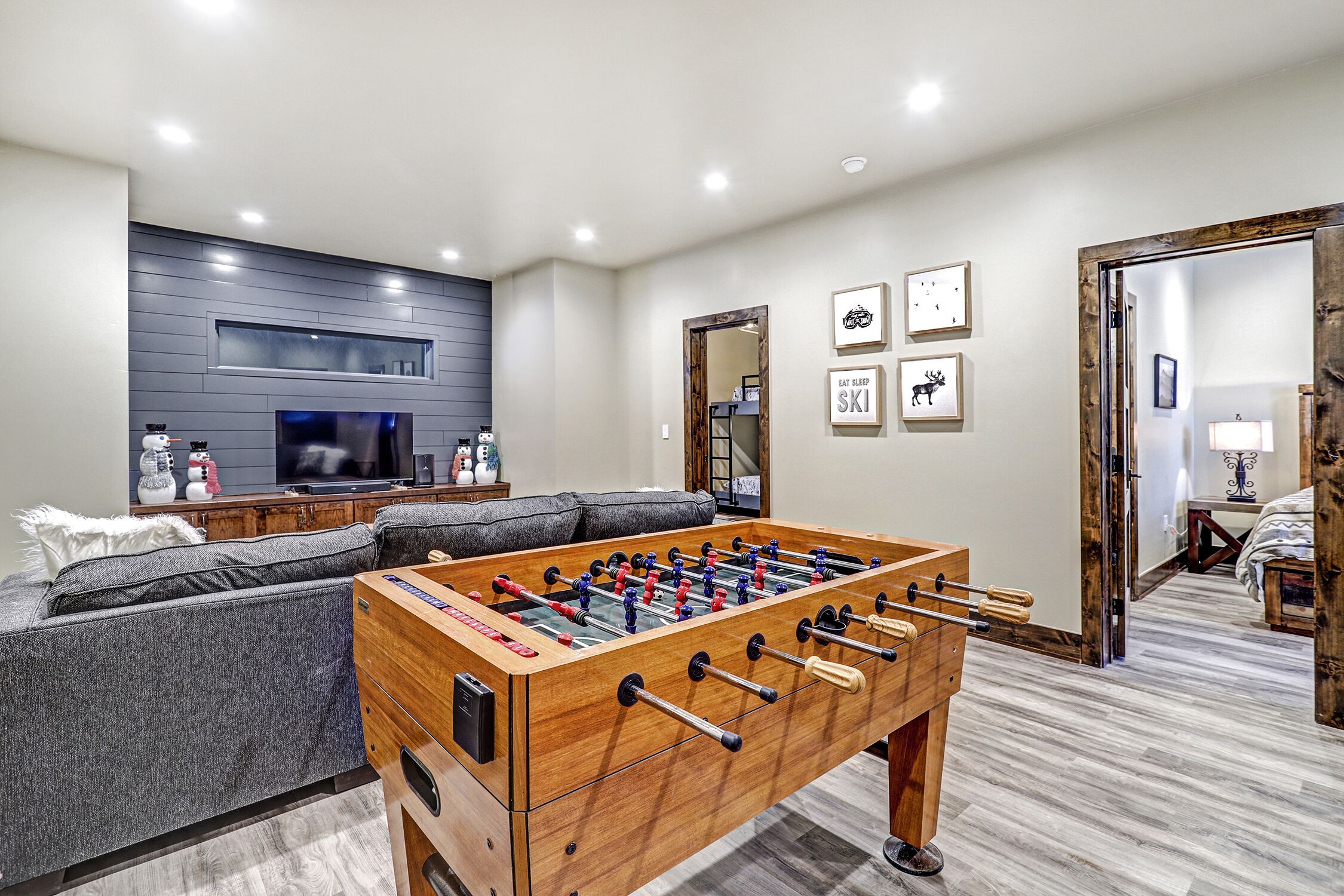 A living room with a foosball table, a gray sofa, a flat-screen TV, and a fireplace.