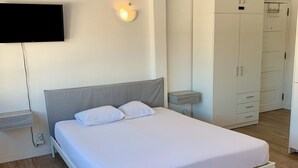 Une chambre à coucher comprenant un lit, une armoire, un téléviseur fixé au mur et une table de chevet.