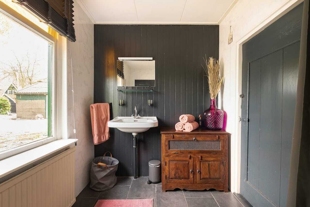 Een badkamer met raam, wastafel, spiegel en houten kast.