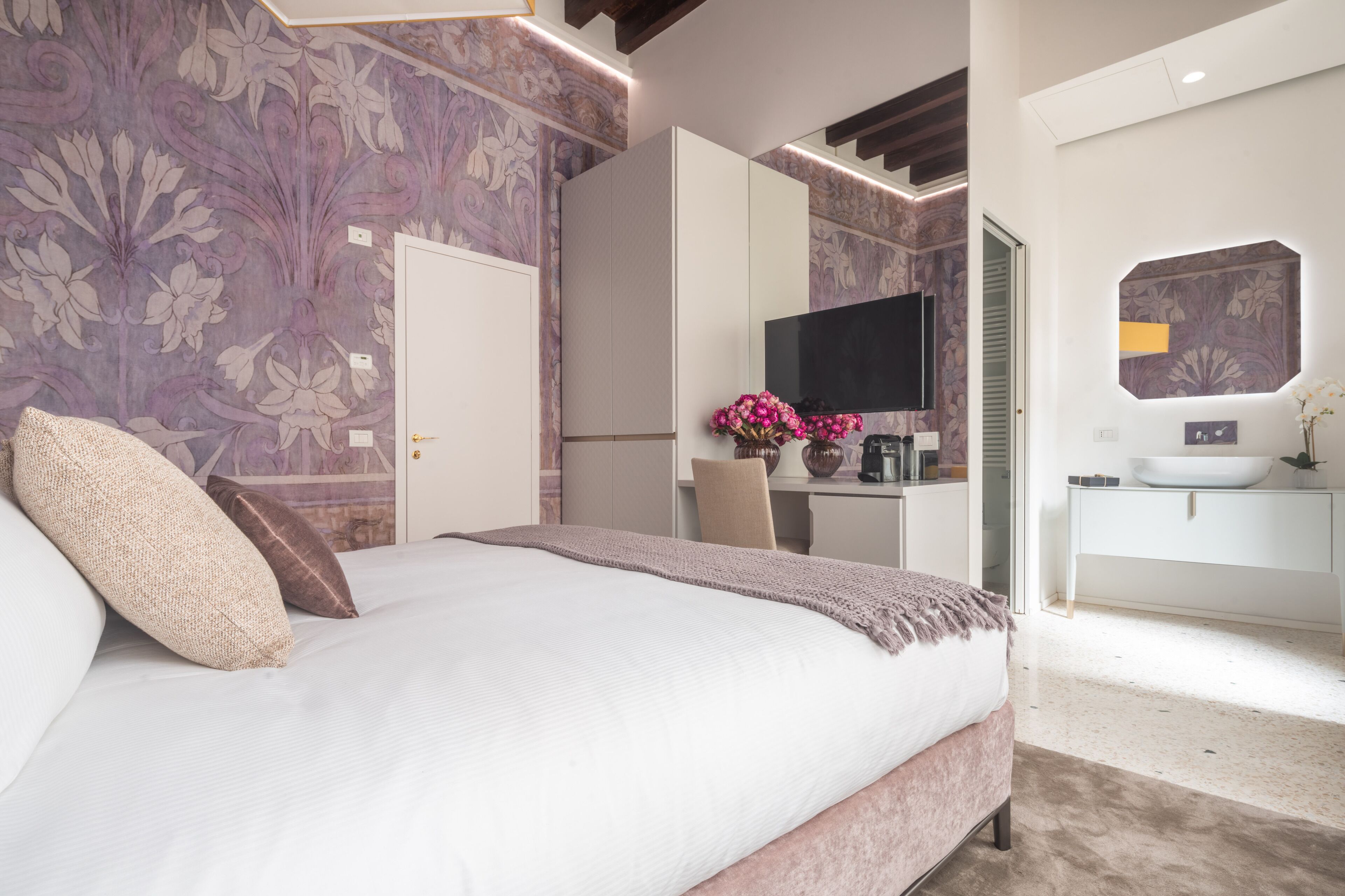 Een slaapkamer met een groot bed, een bureau, een televisie en een badkamer met een wastafel en spiegel.