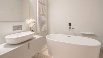 Un baño moderno con una bañera independiente, un espejo grande y un lavabo blanco.
