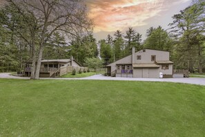 A two-story house with a porch and a fenced yard, surrounded by trees.