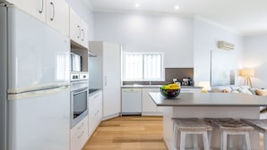 Una cucina moderna con mobili bianchi, forno integrato e lavastoviglie. Una finestra lascia entrare la luce naturale, e c'è una ciotola di frutta sul bancone.