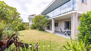 Une maison moderne dotée d’un vaste jardin, d’une terrasse avec mobilier d’extérieur et d’une grande baie vitrée.