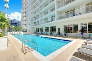 A swimming pool with lounge chairs and a building with balconies.