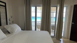 A bedroom with a large bed, a view of the ocean through a sliding door, and a door to the right.