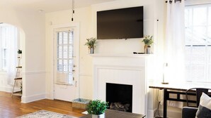 Una sala de estar con chimenea, un televisor de pantalla plana montado encima y una mesa de centro de madera con una planta.