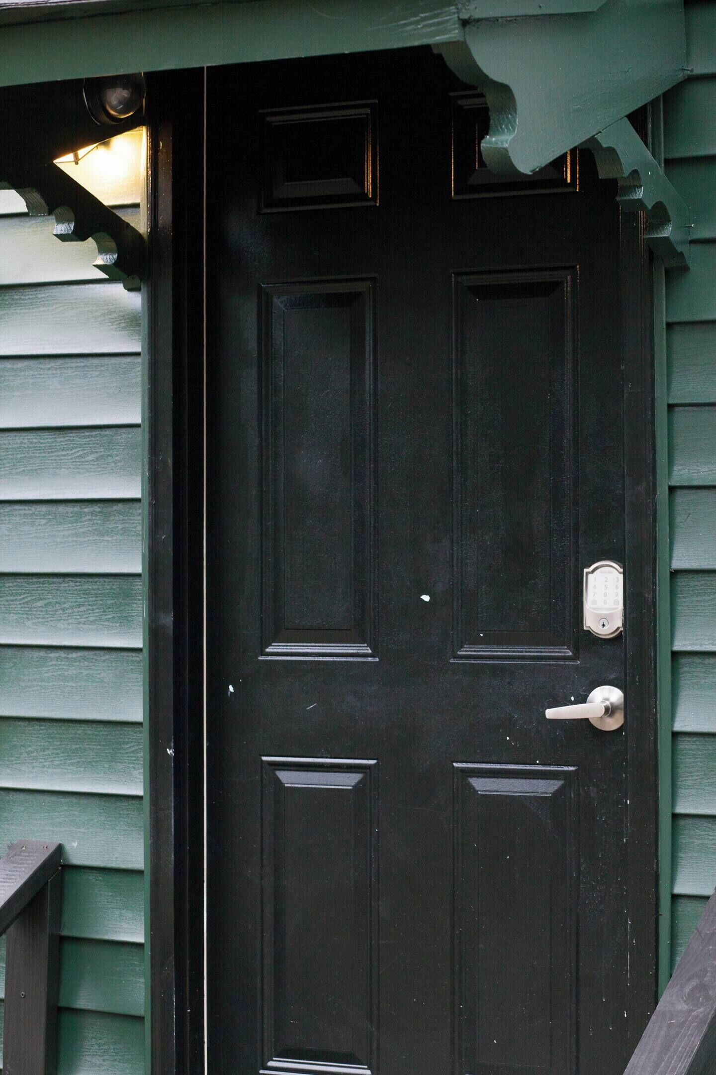 A black door with a metal handle and a keyhole, set in a green wooden frame.