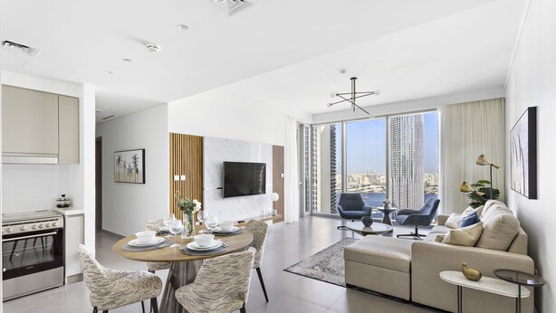 A modern living room with a sofa, a dining area with a table and chairs, a kitchen with an oven, and a large window with a city view. - WelHome - Luxe Apartment With Incredible View on Dubai Creek (Dubai)