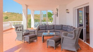 A covered outdoor seating area with wicker furniture, a glass-top table, and a view of the landscape. - Beautiful view, up to 12 p., heated pool & relax pool, panorama, wifi, airco. (Torrox)