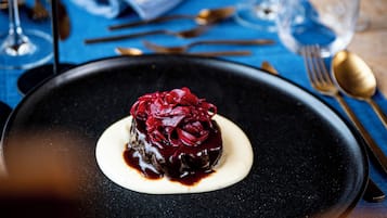 A dessert on a black plate with a blue tablecloth, accompanied by a folded napkin, cutlery, and wine glasses.