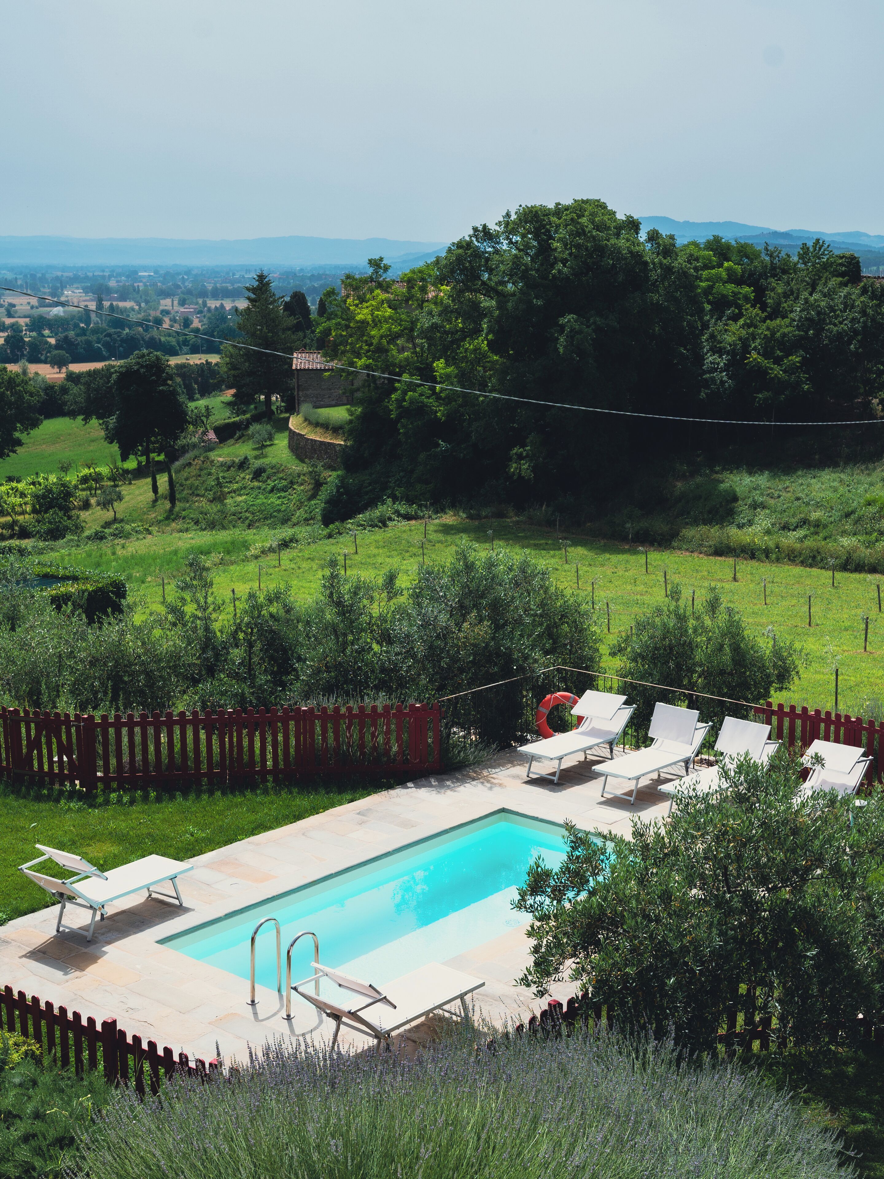 A rectangular swimming pool with a wooden deck, surrounded by a red wooden fence.