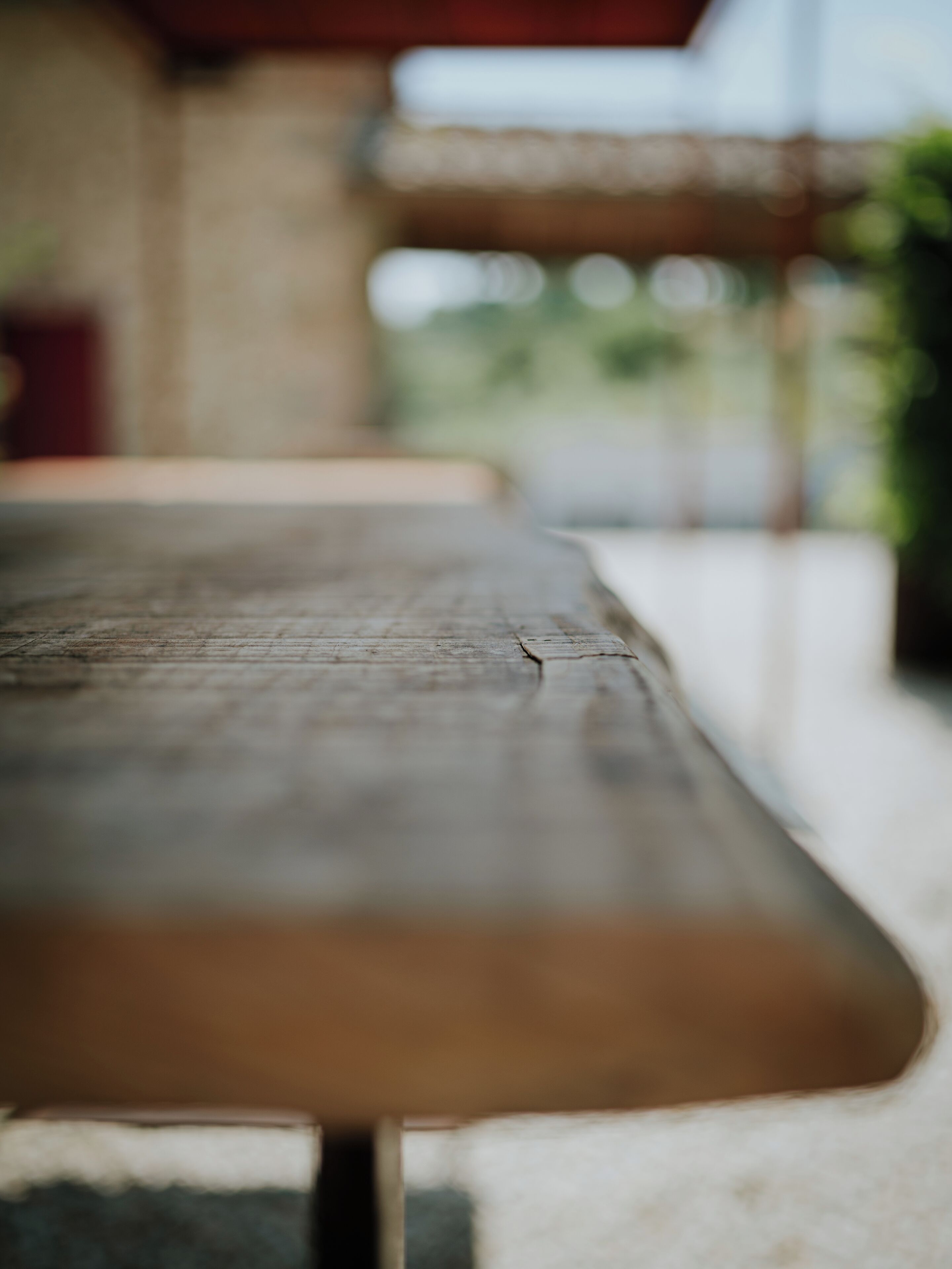 A wooden bench with a slatted seat and backrest, positioned outdoors with a blurred background suggesting a natural setting.