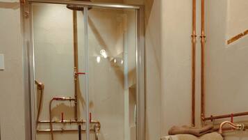 A bathroom with a glass shower enclosure, copper pipes, a sink, and a wooden cabinet.