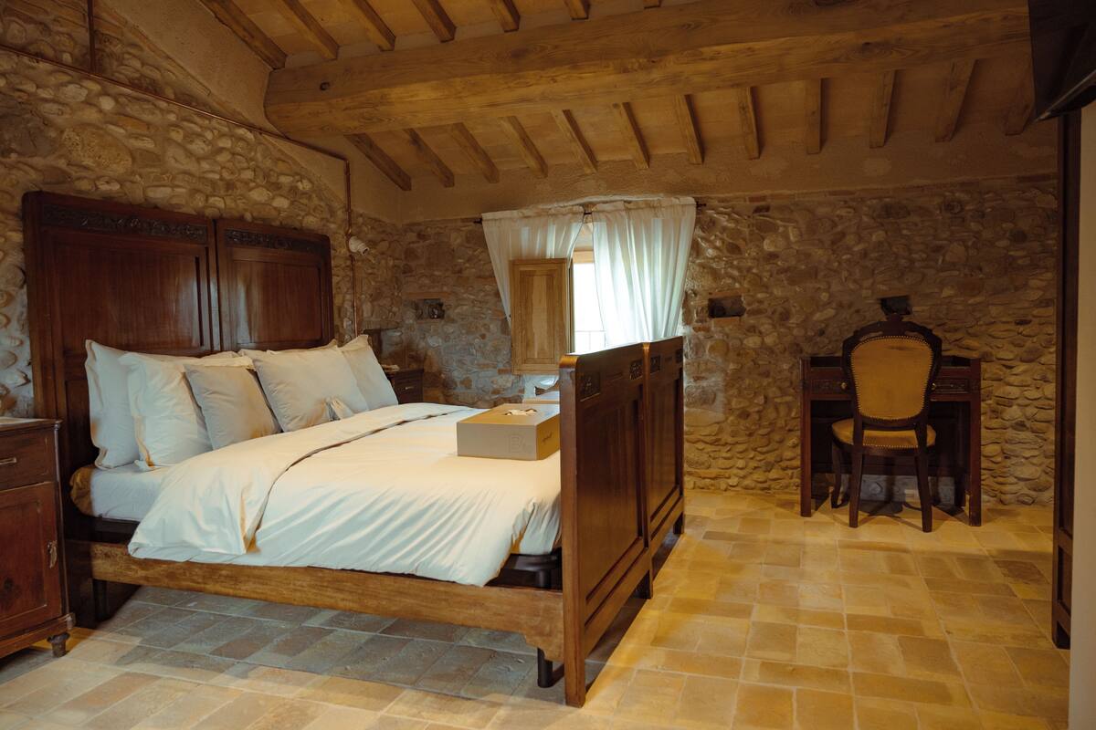 A bedroom with a stone wall, wooden bed, and a desk with a chair.