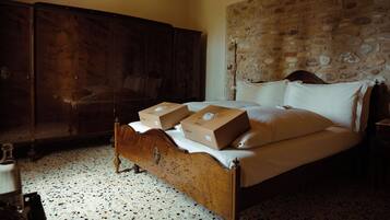 Un dormitorio con una cama, dos cajas sobre la cama, un armario de madera y una pared de piedra.