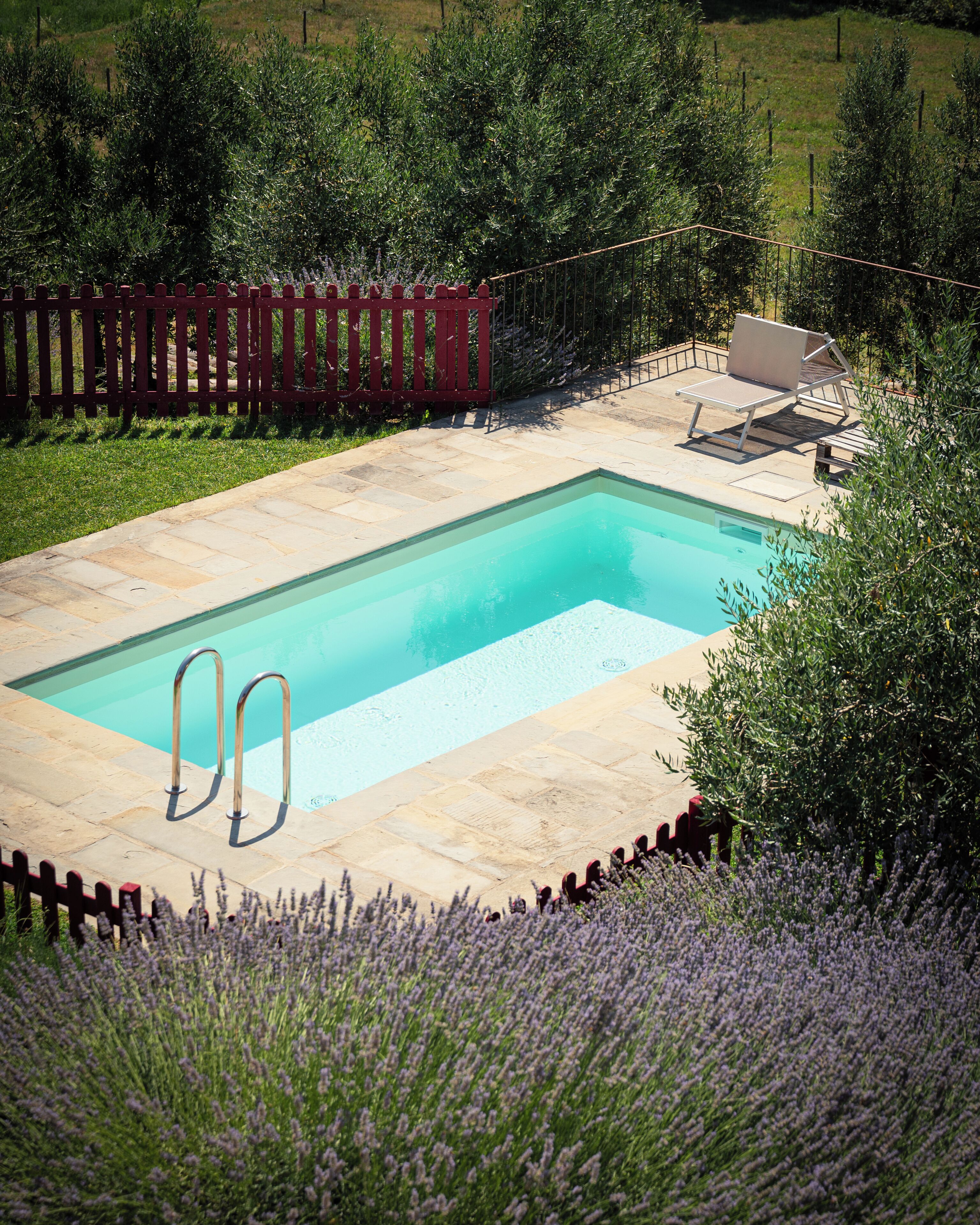 Una piscina rectangular amb una tanca vermella i una cadira de relax.
