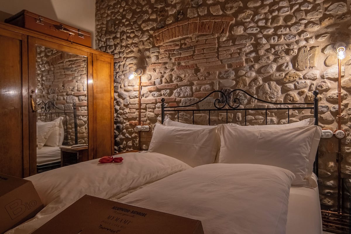 A bedroom with a stone wall, a wooden wardrobe, a bed with white linens, and a box labeled "Bio".