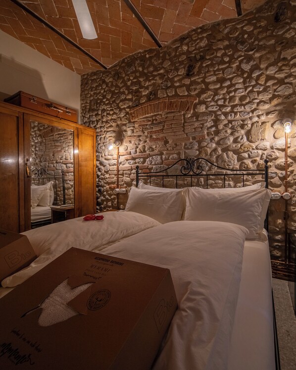 Un dormitorio con pared de piedra, un armario de madera, una cama con ropa de cama blanca y una caja etiquetada 