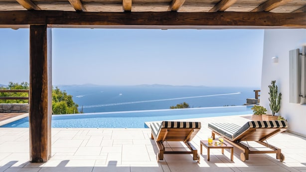 A wooden pergola over a swimming pool with lounge chairs and a view of the sea. - Villa Olivia Mykonos (Mykonos)