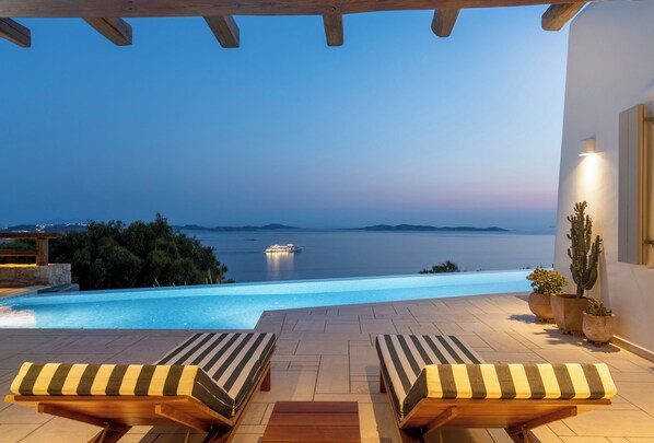Ein Poolbereich mit zwei Liegestühlen, Blick auf das Meer und einer Kakteenpflanze.