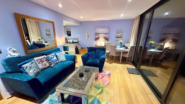 A living room with a blue sofa, a coffee table, and a dining area with a table and chairs. - Westward Ho-rizon View 9 (Westward Ho!)