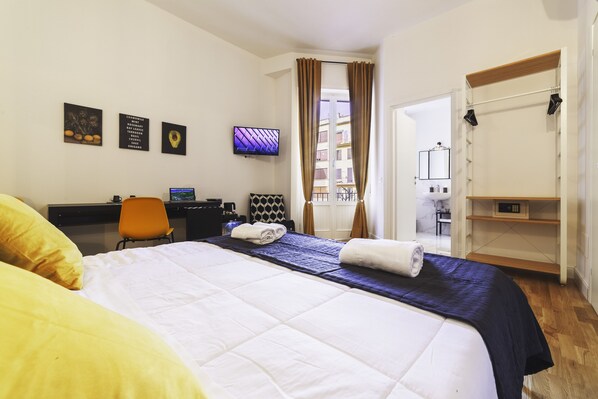 A hotel room with a bed, a desk with a computer, a TV, and a wardrobe.