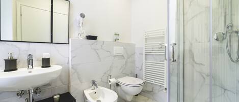 Une salle de bain avec un lavabo blanc, un bidet, des toilettes et une douche à parois de verre.