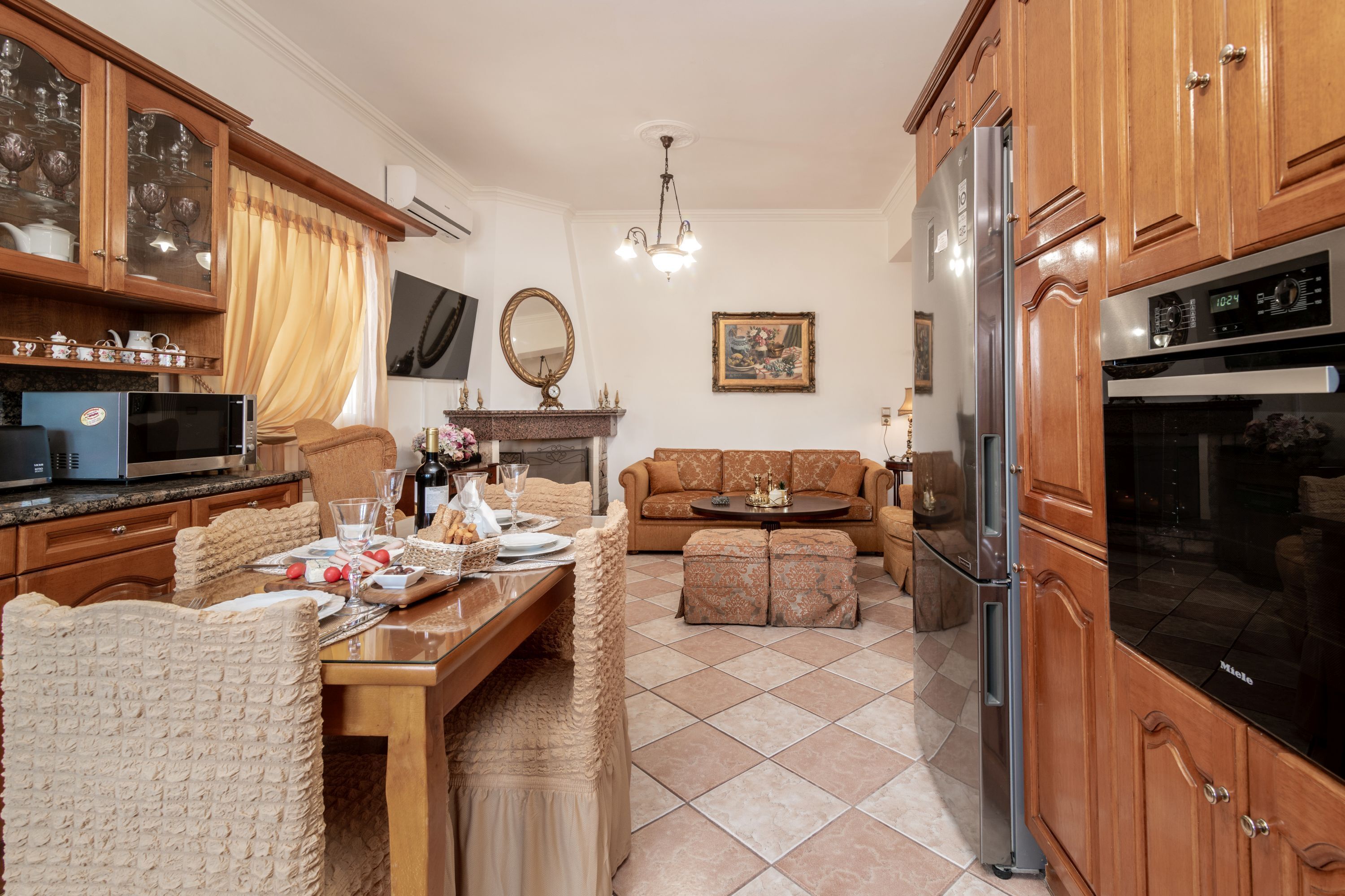 Una cuina amb armaris de fusta, una taula de dinar preparada per a quatre i una zona de estar amb un sofà i taula de centre.
