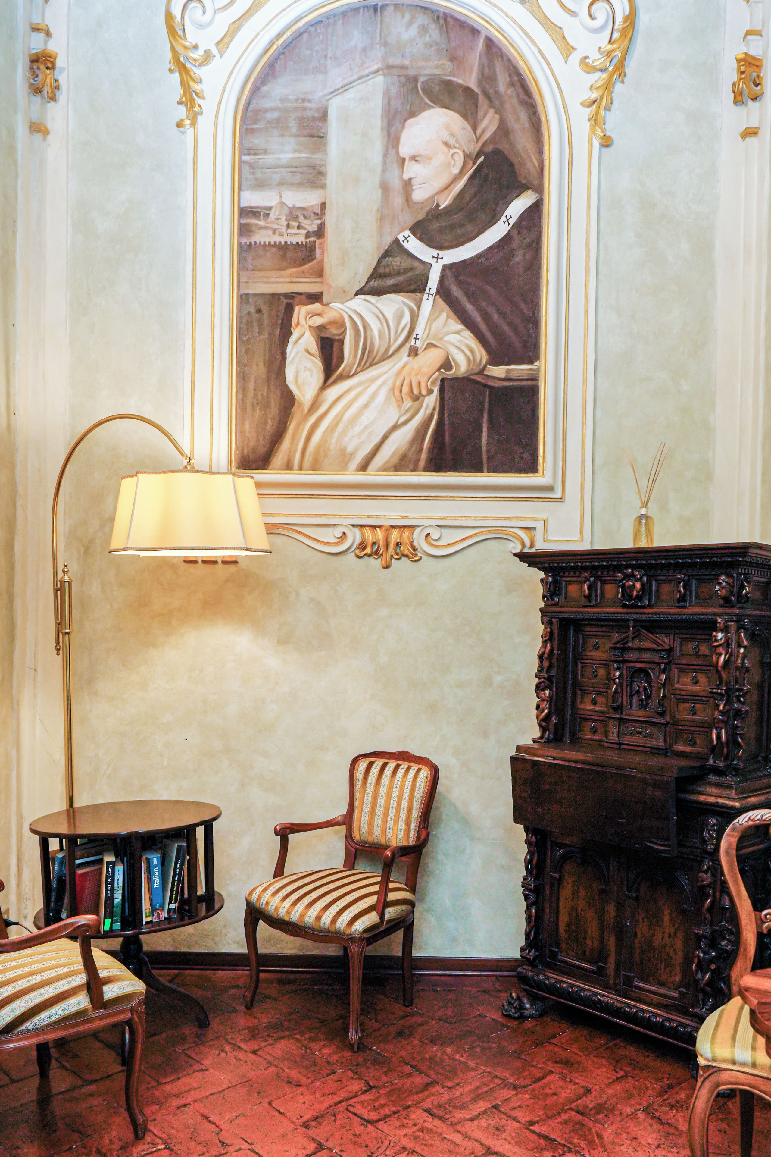 Una habitación con un retrato enmarcado, una lámpara, una silla y un mueble de madera.