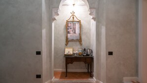 A hallway with a framed picture on a wall, a small table with a coffee maker, and a tiled floor. - Dimora del Cardinale - Residenza d'epoca (Florence)