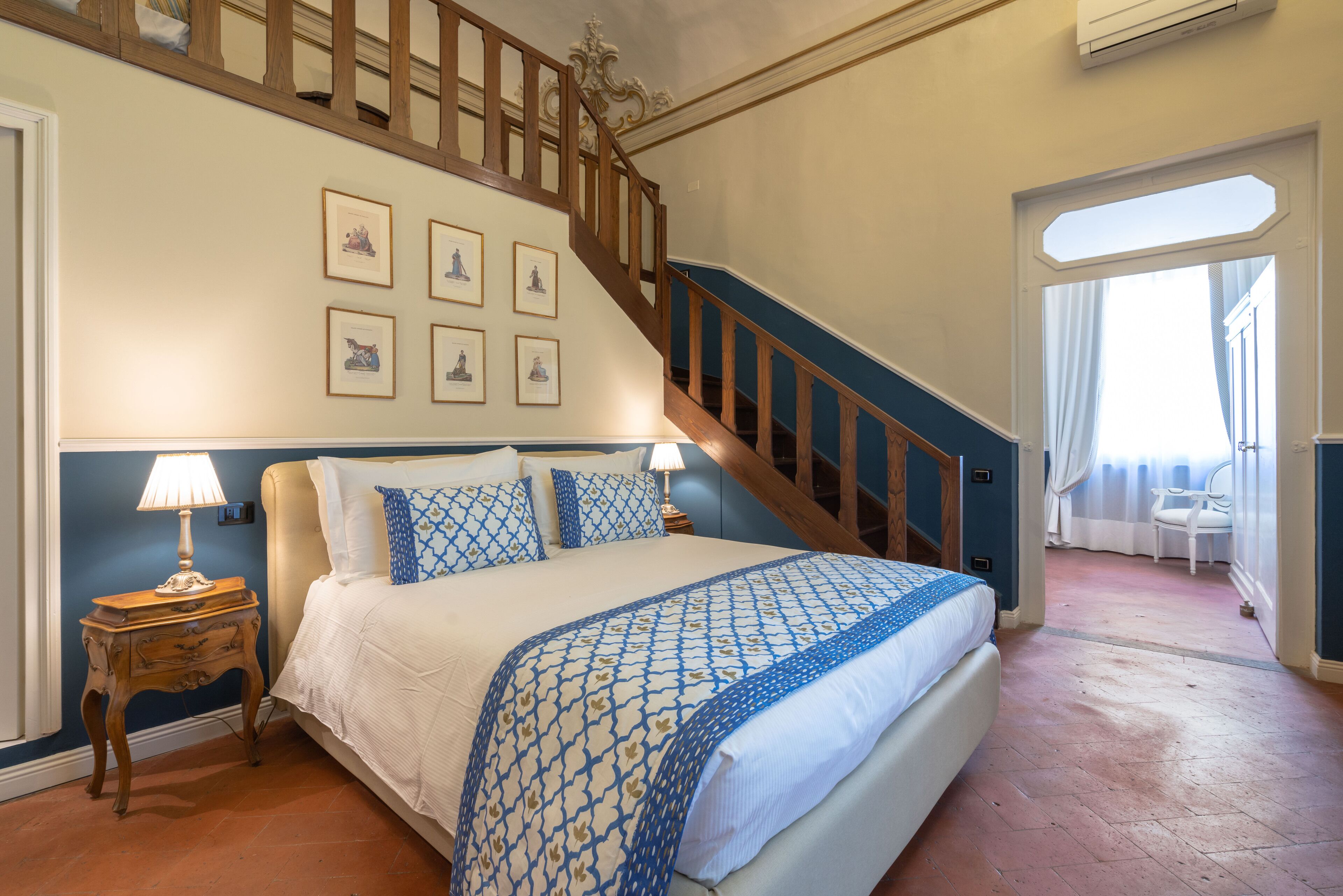 A bedroom with a large bed, a wooden staircase, and framed pictures on the wall.