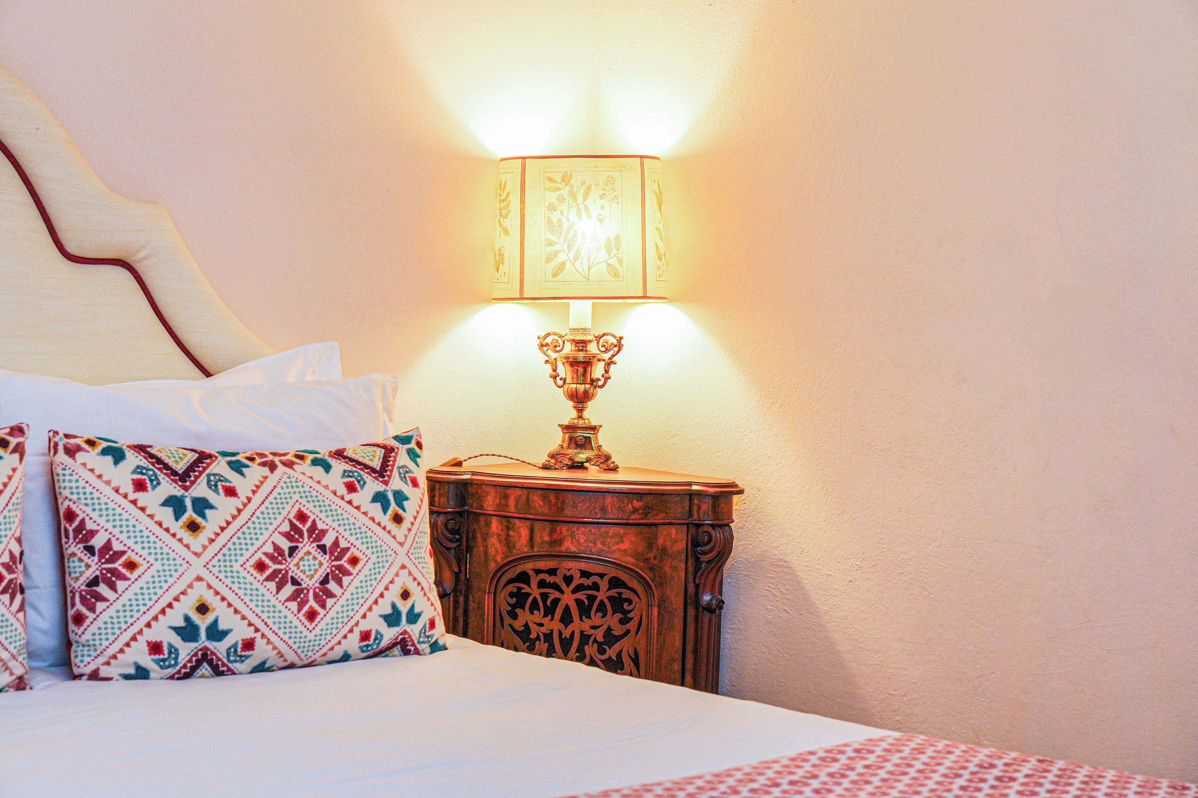 Een keurig opgemaakt bed met gestreepte kussens, een nachtkastje met een lamp en een decoratieve wand.